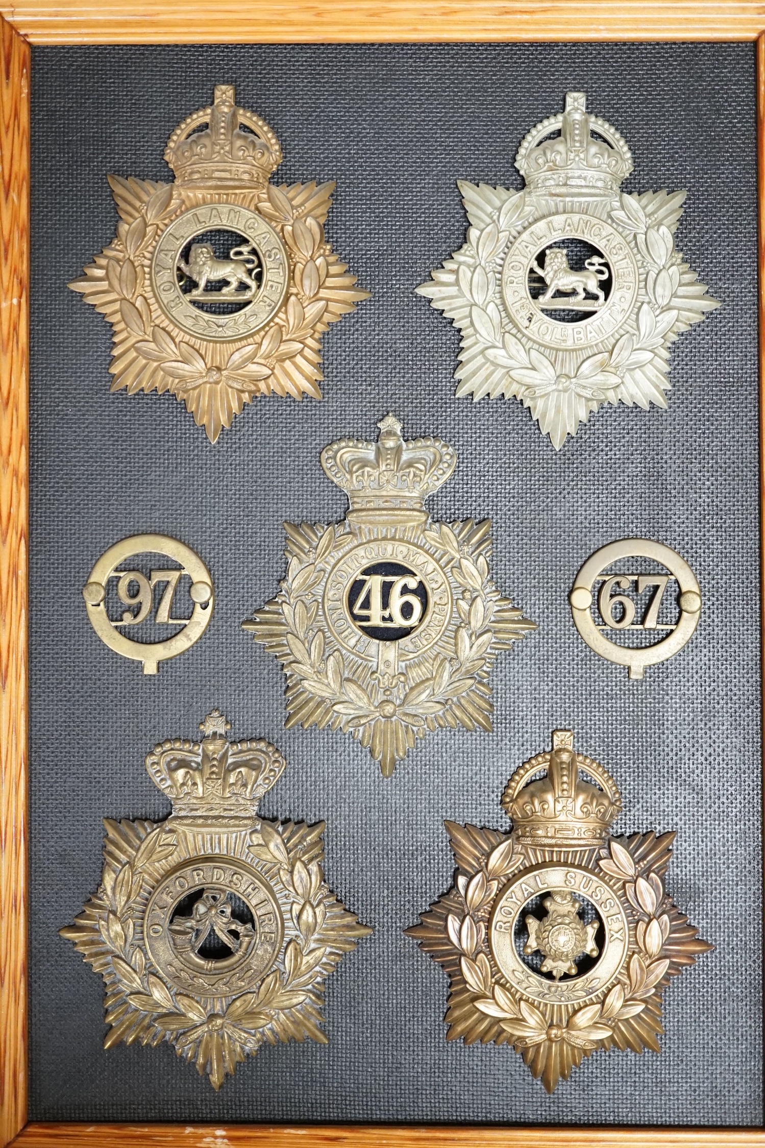 Five military helmet plates and two other centre badges mounted on a board, including; the Royal Lancashire Regiment, the Royal Lancashire 1st Volunteer Battalion, the Oxfordshire Regiment, the Royal Sussex Regiment, etc